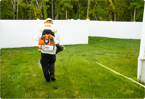 View from behind of a Pest control person spraying in a fenced off backyard.